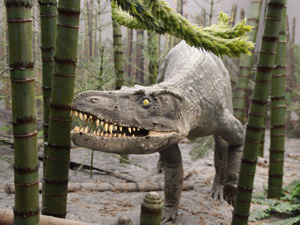 A model of a prehistoric predatory reptile wandering through a forest of horsetail trees with bamboo-like trunks