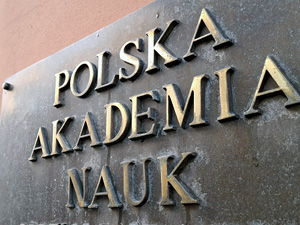 A brass plaque with the words Polish Academy of Sciences visible at an angle, attached to the wall of a building